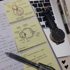 a watch, pen and notebooks on a desk next to a laptop computer with notes