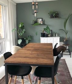 a dining room table and chairs with plants on the wall behind it in front of a window