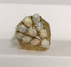 Multiple opals are arranged in a pear shaped setting in a 14 karat yellow gold mounting.  The ring design is very open and light.  The ten opals are well matched and set in four prong settings.  The shank tapers to 3 mm in the back.  This ring is preowned and in good condition. 14k Yellow Gold Pear-shaped Opal Ring, Yellow Gold Pear-shaped Opal Ring, Yellow Gold Ring, Shape Design, Yellow Gold Rings, Rings Statement, Pear Shaped, Prong Setting, Ring Designs