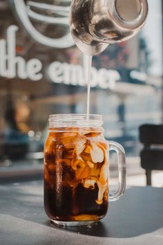 iced coffee being poured into a mason jar on a table in front of the cafe