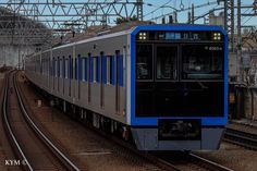 a blue and silver train traveling down tracks next to power lines in an industrial area