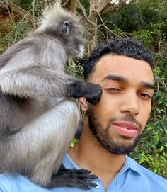 a man holding a monkey on his shoulder in front of trees and bushes with another monkey sitting on top of him