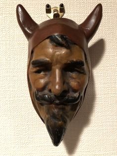 a wooden mask with horns and a mustache on it's head is mounted to the wall