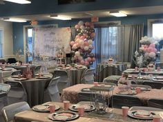 a room filled with tables and chairs covered in pink, white and silver balloons hanging from the ceiling