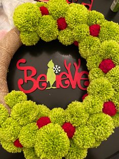 a green wreath with red pom - poms and the words believe on it