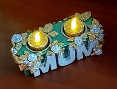 two lit candles sitting on top of a wooden table with the word mum spelled out