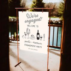 a welcome sign for an engagement party with wine glasses and champagne bottles on the table