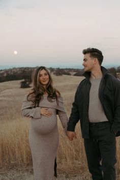 a pregnant couple holding hands while standing in a field