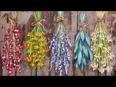 four different colored flowers are tied to the side of a wooden wall with twine