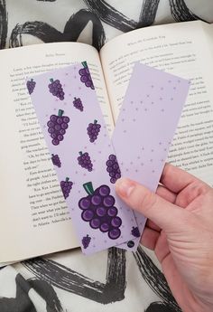 a person holding an open book with paper cut out of it and grapes on the pages