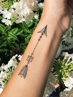 a woman's arm with an arrow tattoo on it and flowers in the background