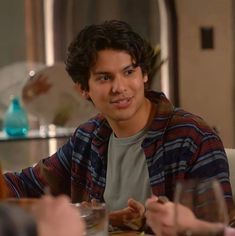 a young man sitting at a table in front of two other people with wine glasses