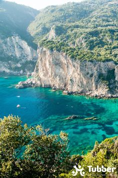 the water is crystal blue and clear with green trees on both sides, and cliffs in the background