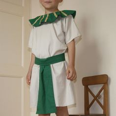 a young boy dressed in roman costume standing next to a chair