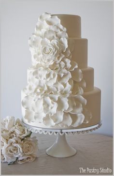 a three tiered wedding cake with white flowers on the top and bottom, sitting on a table