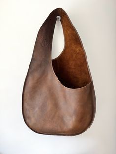 a brown leather bag hanging on the wall with a hook in it's center