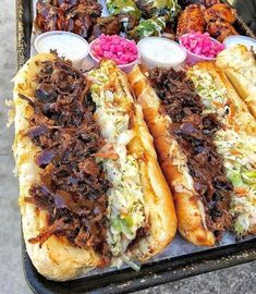 two long sandwiches with meat, coleslaw and other condiments on a tray