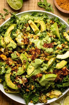 a white bowl filled with greens and avocado on top of a wooden table