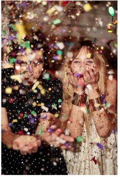 two people standing in front of confetti falling from their hands and covering their faces