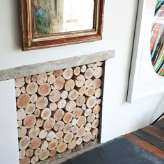 a fire place with logs stacked on top of it next to a painting and mirror