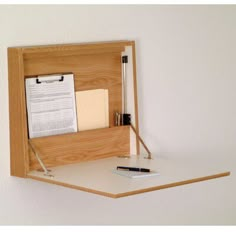 a wooden desk with a pen, notepad and clipboard attached to the wall