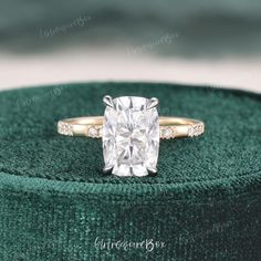 an engagement ring with a cushion cut diamond in the center on a green velvet box