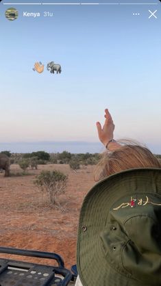 a woman in a safari hat is looking at elephants flying over her head and holding up her hand