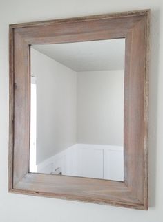 a wooden mirror hanging on the wall above a sink in a room with white walls