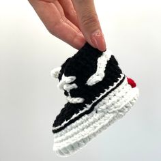 a hand holding a crocheted black and white tennis shoe