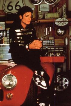 michael jackson sitting on top of an old red car in front of a store display