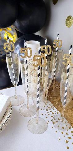 champagne flutes with black and white striped paper straws are on a table in front of gold confetti