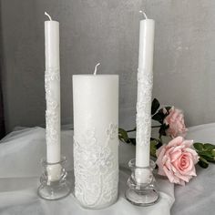 three white candles sitting next to each other on top of a table with pink flowers