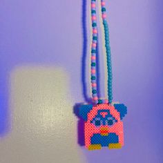 a beaded necklace with a bear hanging from it's side on a purple wall