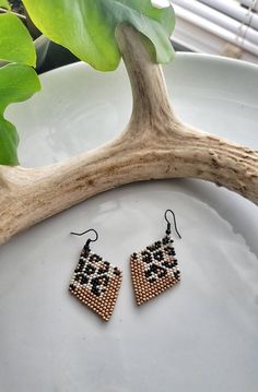 a pair of beaded earrings sitting on top of a plate next to a plant