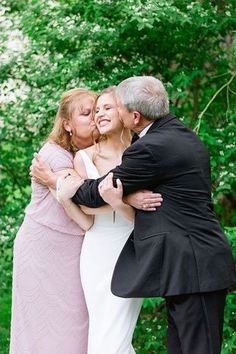 an older man and woman hugging each other in front of some green trees at their wedding