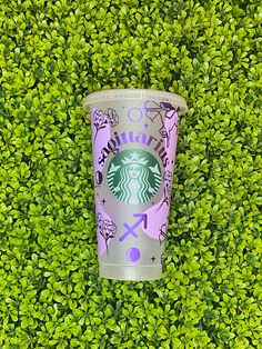 a starbucks cup sitting on top of a lush green hedge covered in leaves and flowers