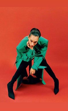 a woman sitting on the ground in black pants and a green shirt with long sleeves