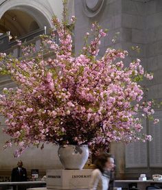 a large vase filled with pink flowers sitting on top of a white table next to a woman