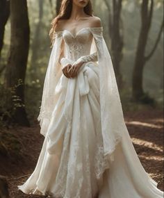 a woman in a white wedding dress standing in the woods with her arms wrapped around her shoulders