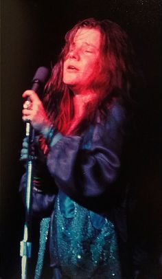 a woman with long hair holding a microphone in her hand and singing into the microphone