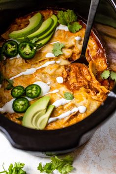 a crock pot filled with chicken enchiladas and avocado