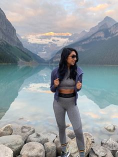 a woman standing on top of a rock next to a lake