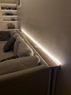 a couch with pillows on it is lit up by a strip of light in the corner