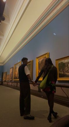 a man and woman standing next to each other in front of paintings on the wall