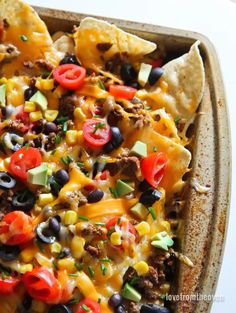 nachos with beef, black olives, tomatoes and corn in a casserole dish