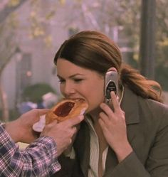 a man and woman eating hotdogs while talking on their cell phones