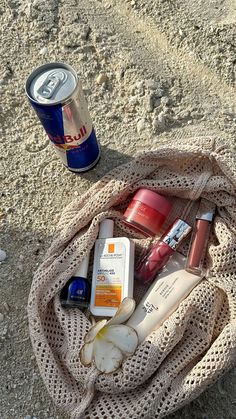 the contents of a beach bag sitting on the sand next to a can of soda