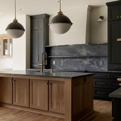 a large kitchen with black cabinets and marble counter tops, two pendant lights over the island