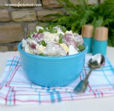 a blue bowl filled with food sitting on top of a table next to two spoons