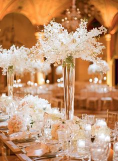 tall vases filled with white flowers and greenery on top of a long table